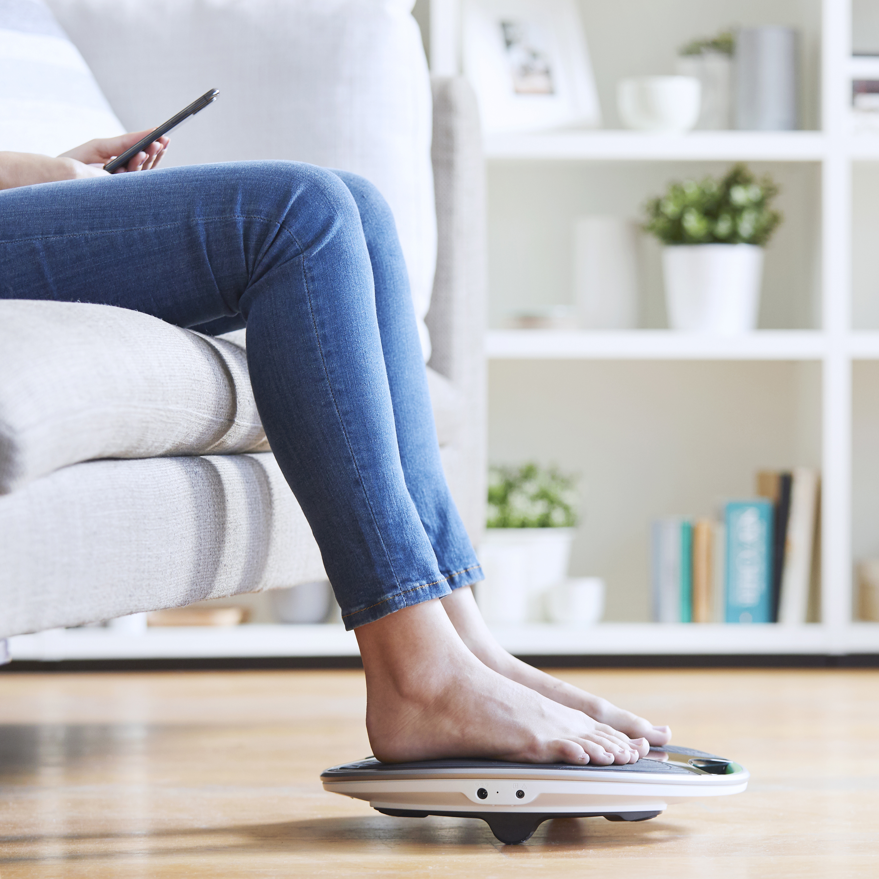 Person sitting on couch using a foot muscle stimulation device
