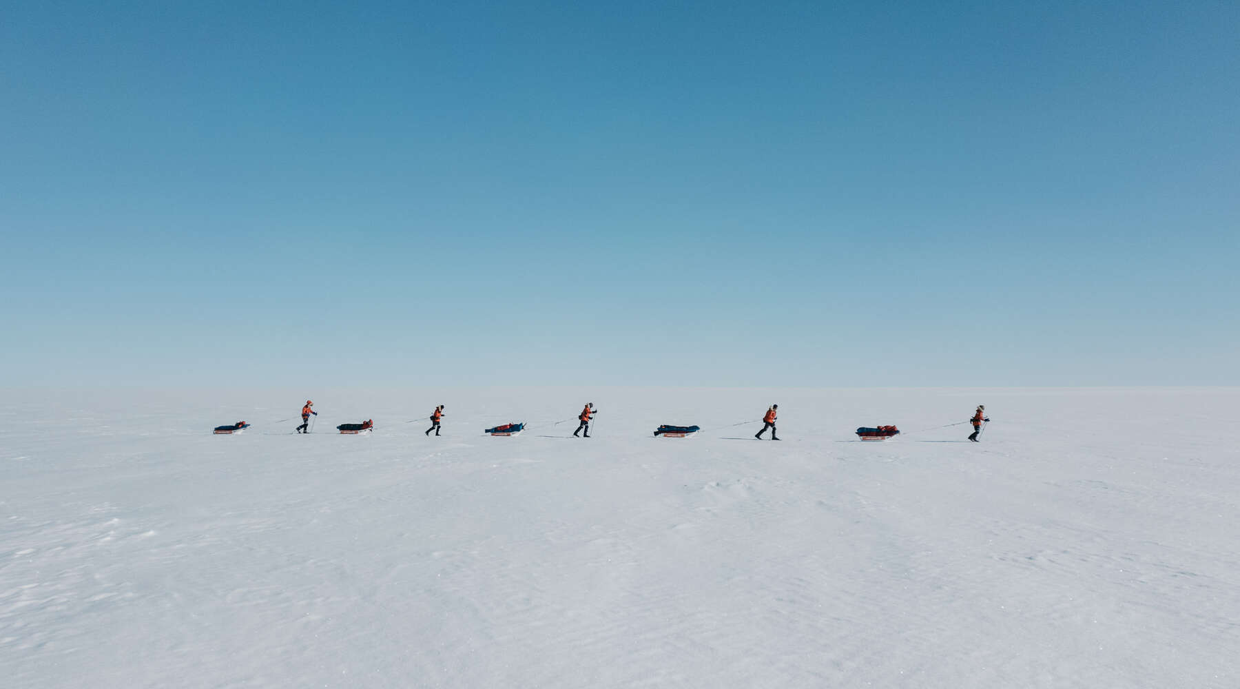 people walking across snow with sleds of equipment