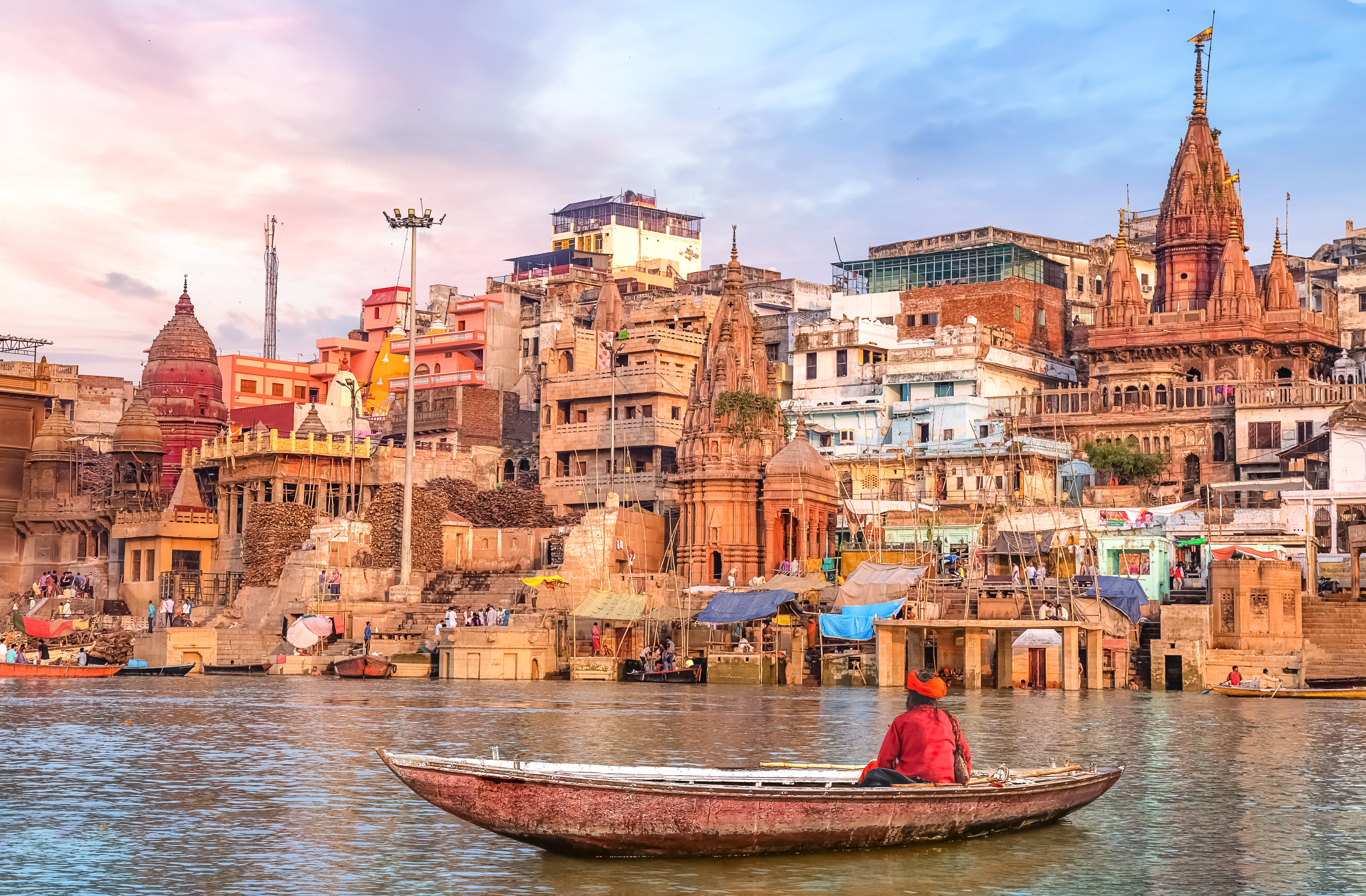 Hindu sadhu sitting on a boat overlooking Varanasi city architecture at sunset